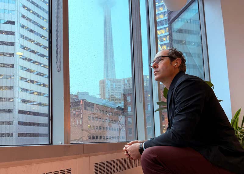 Joel Varty looking out a window with the CN tower in the background
